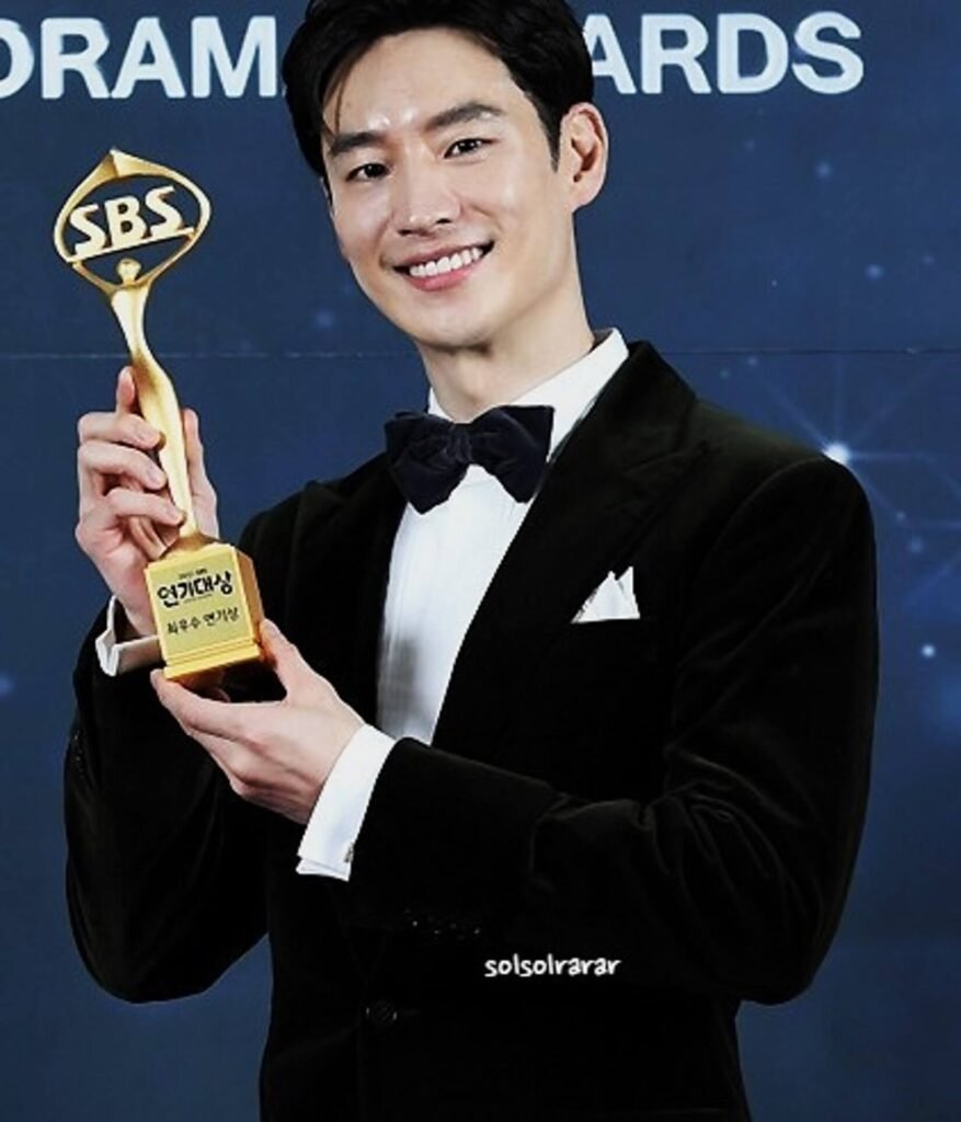Actor Lee Je-hoon smiling brightly while holding a trophy