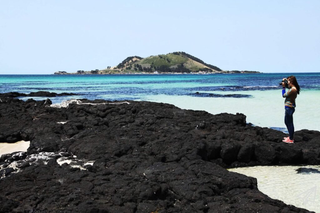 A woman stands on a rocky beach to take a picture