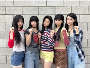 ILLIT members raise one hand and clench their fists to show their determination