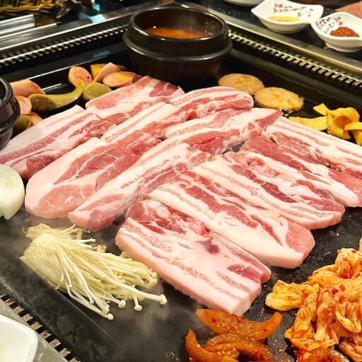 Grilling pork belly, kimchi, and mushrooms on a grill