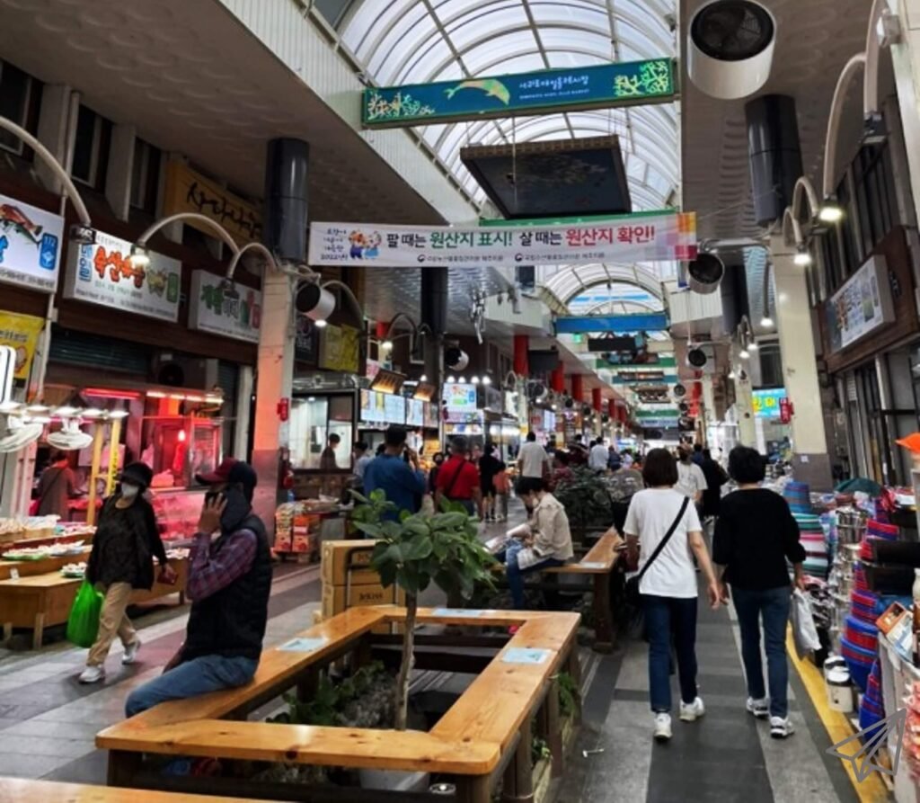 There are shops on both sides of the alley in Seogwipo Market, and people pass by.