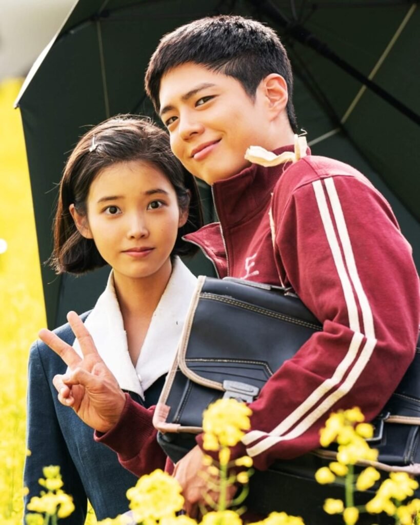 IU and Park Bo-gum standing in a field of rapeseed flowers